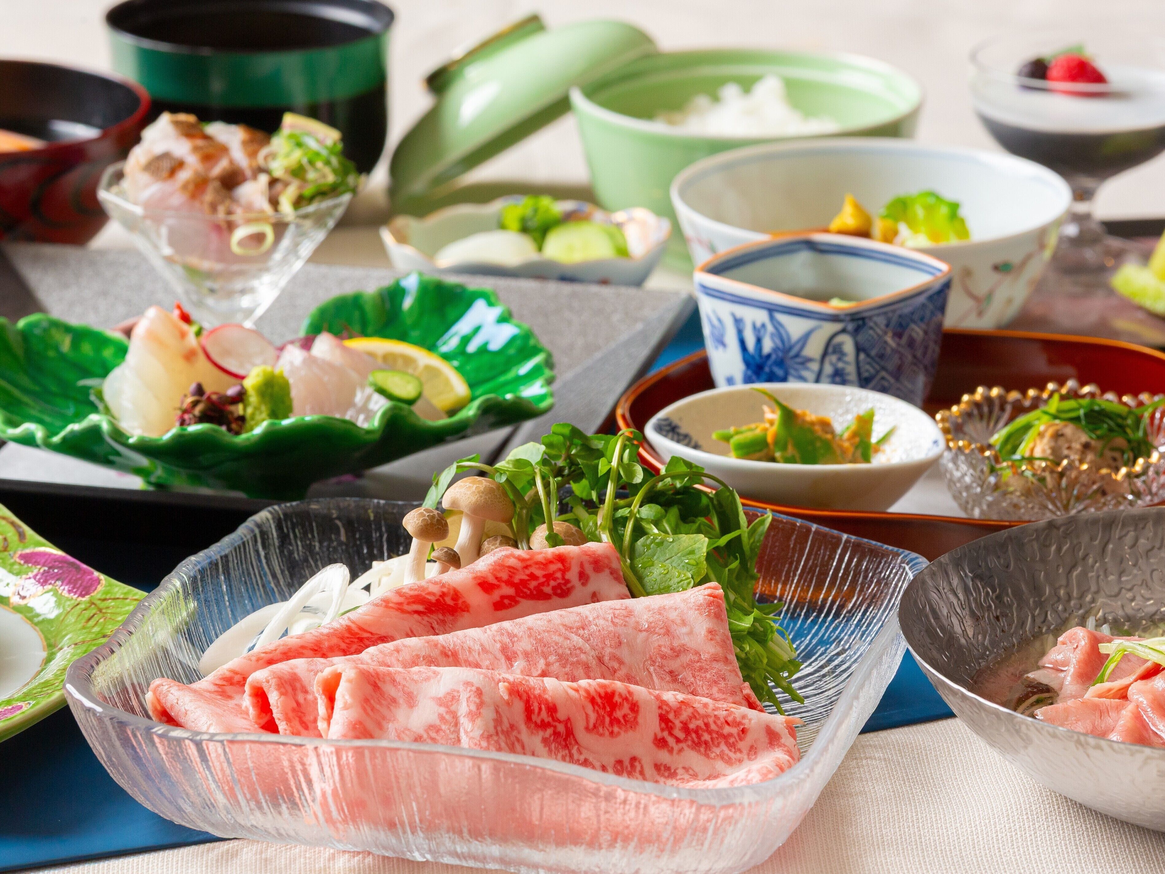 A variety of dishes on a table, including a bowl of sliced meat, a bowl of vegetables, and several other dishes in different bowls.