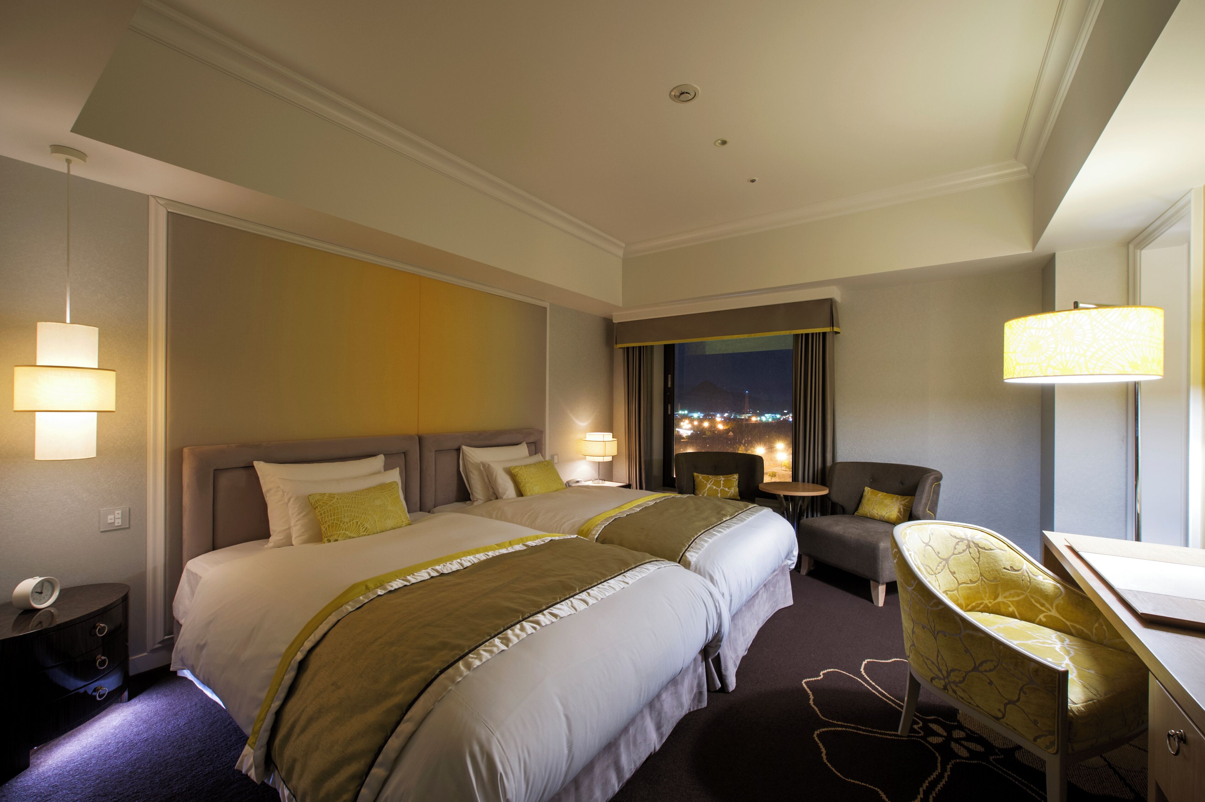 A hotel room with two beds, a desk, a chair, and a view of the city at night.
