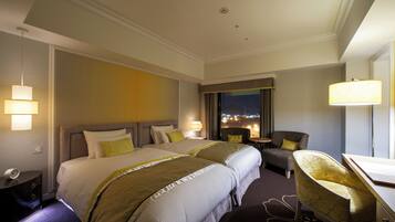A hotel room with two beds, a desk, a chair, and a view of the city at night.