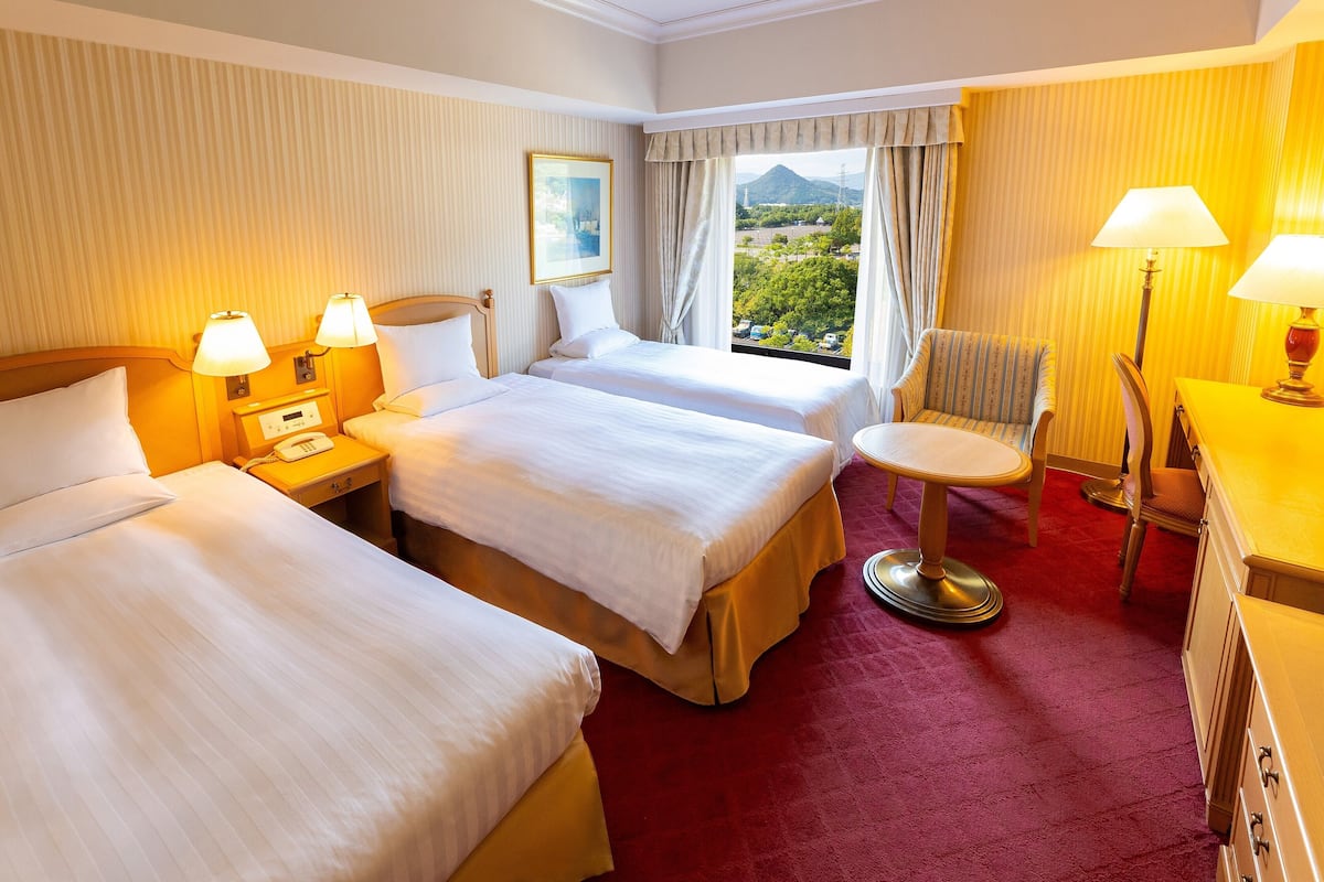Habitación de hotel con dos camas, un escritorio, una silla y vistas a la montaña.