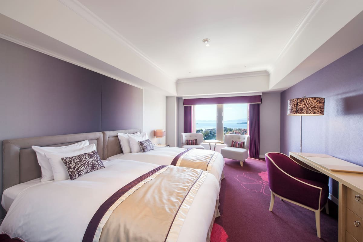 Habitación de hotel con dos camas, un escritorio, una silla y vistas a la ciudad.
