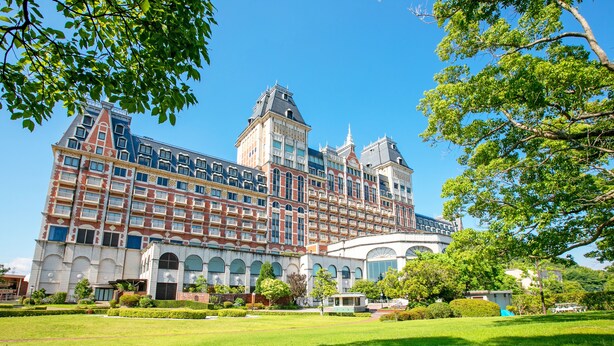 A large, historic building with multiple stories, a prominent central tower, and a well-maintained garden in front. - Hotel Okura JR Huis Ten Bosch (Sasebo)