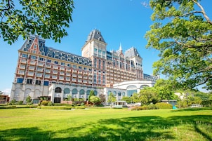 Un edificio grande y con historia, de varias plantas, con una torre central destacada y un jardín bien cuidado al frente.