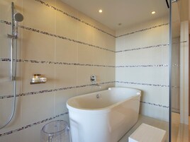 Un baño moderno con una bañera independiente, cabina de ducha con paredes de vidrio y un pequeño cubo de basura.