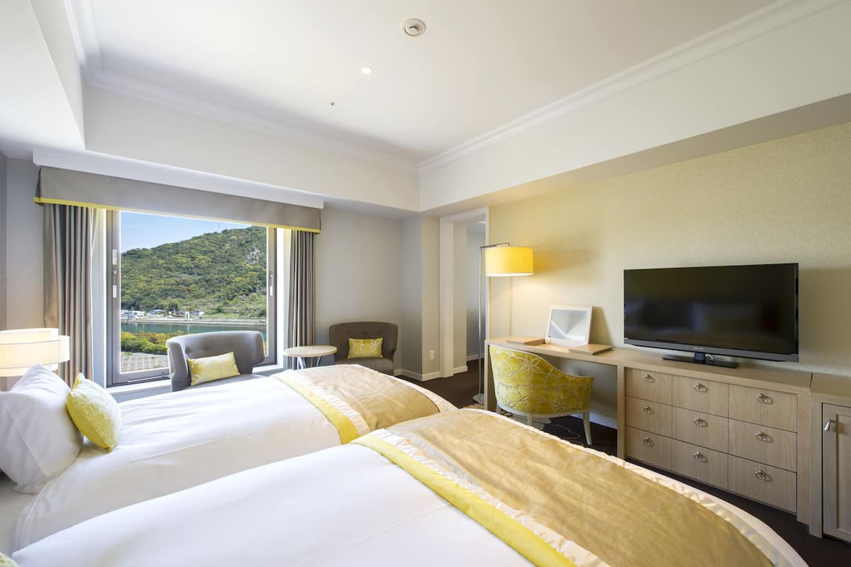 Habitación de hotel con dos camas, televisión, escritorio y vista a un paisaje montañoso.