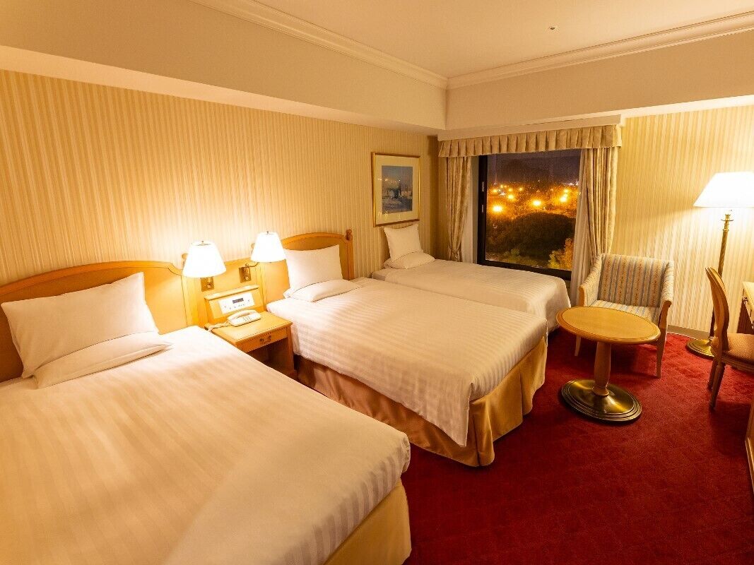 A hotel room with two beds, a small round table, and a chair.