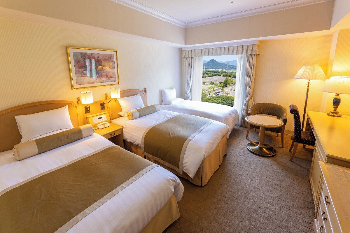 Habitación de hotel con dos camas, un escritorio, una silla y ventana con vista a la montaña.