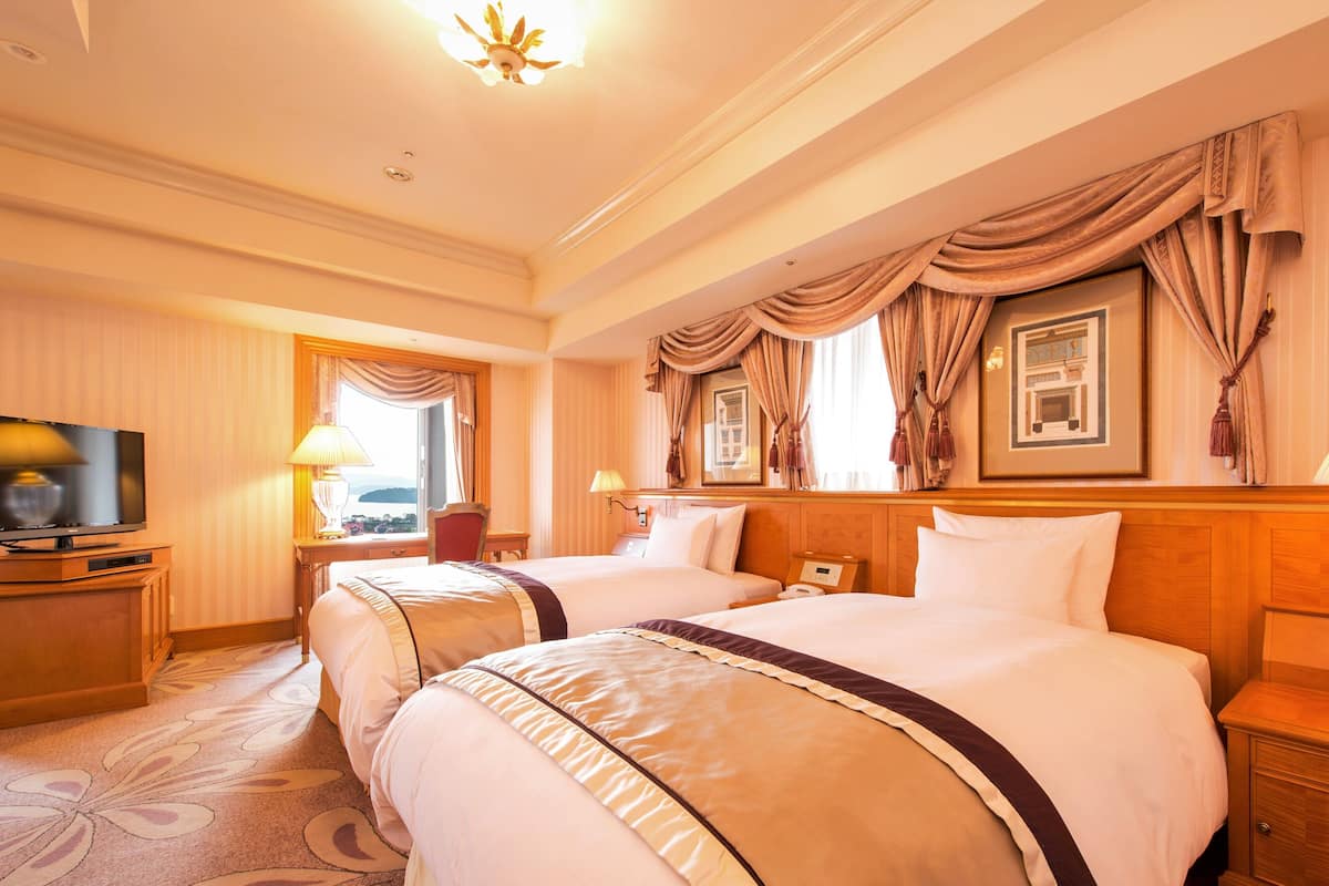 Habitación de hotel con dos camas, televisión, escritorio y ventana con cortinas.