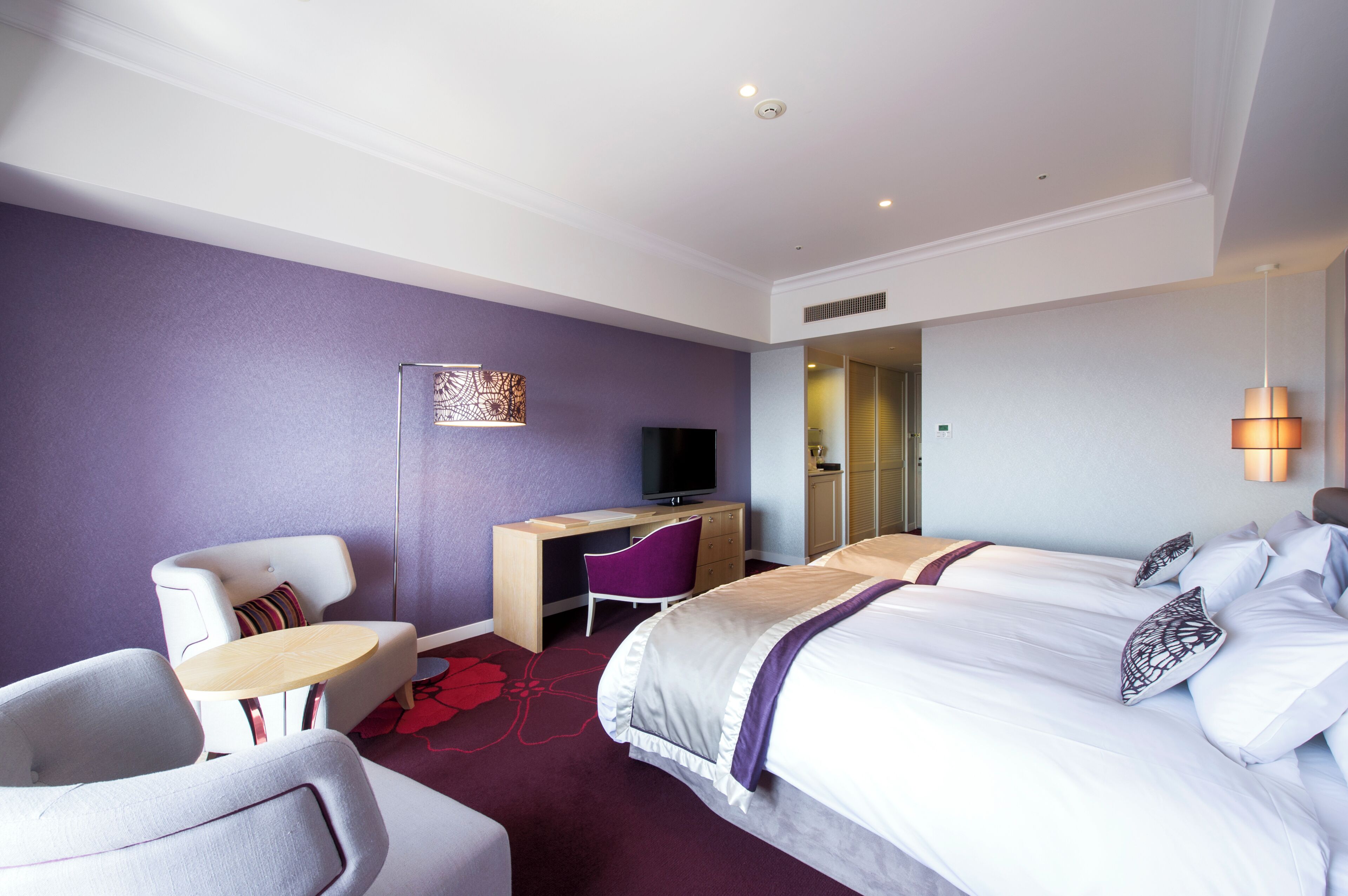 A hotel room with a bed, a desk, a chair, and a television.