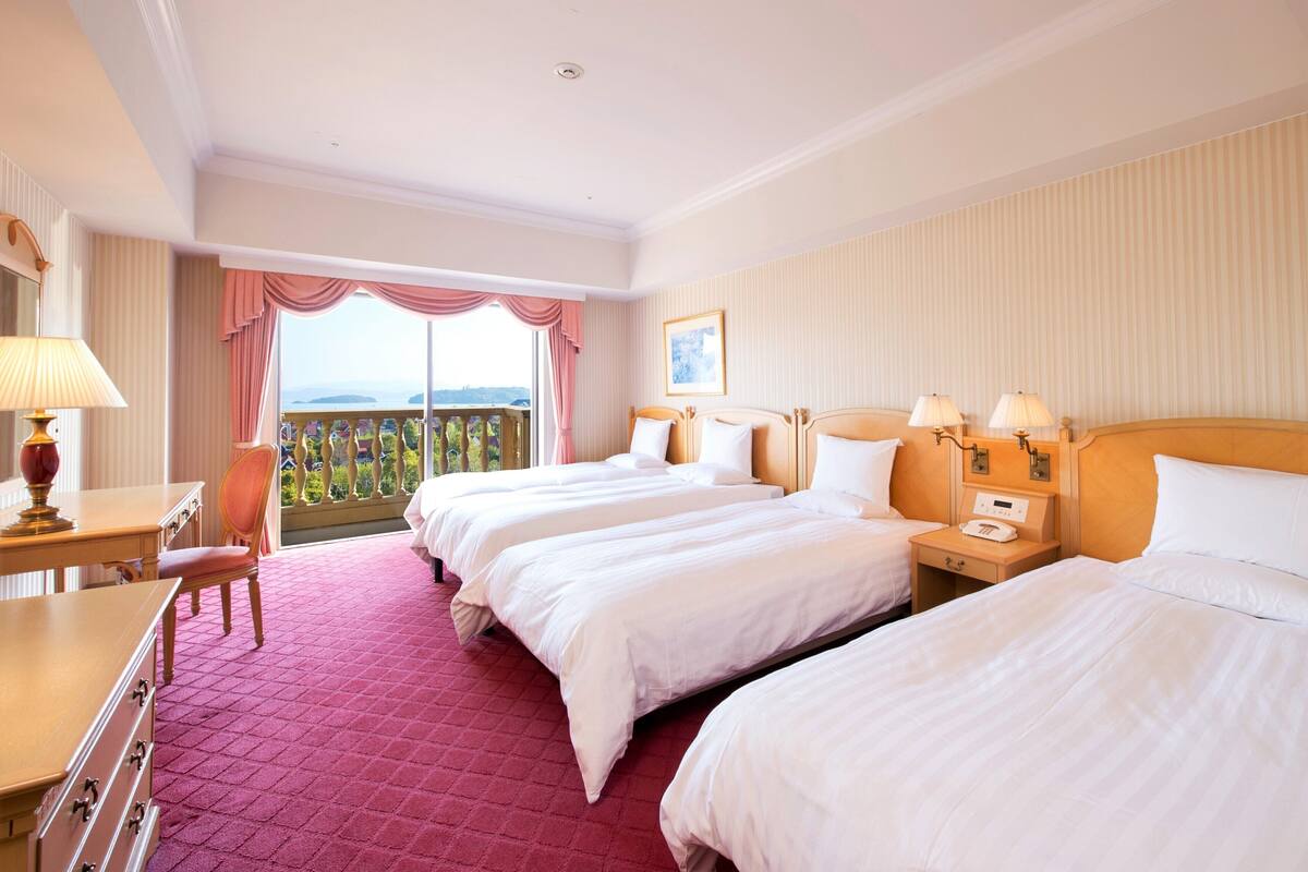 Habitación de hotel con dos camas, un escritorio, una silla y un balcón con vistas.