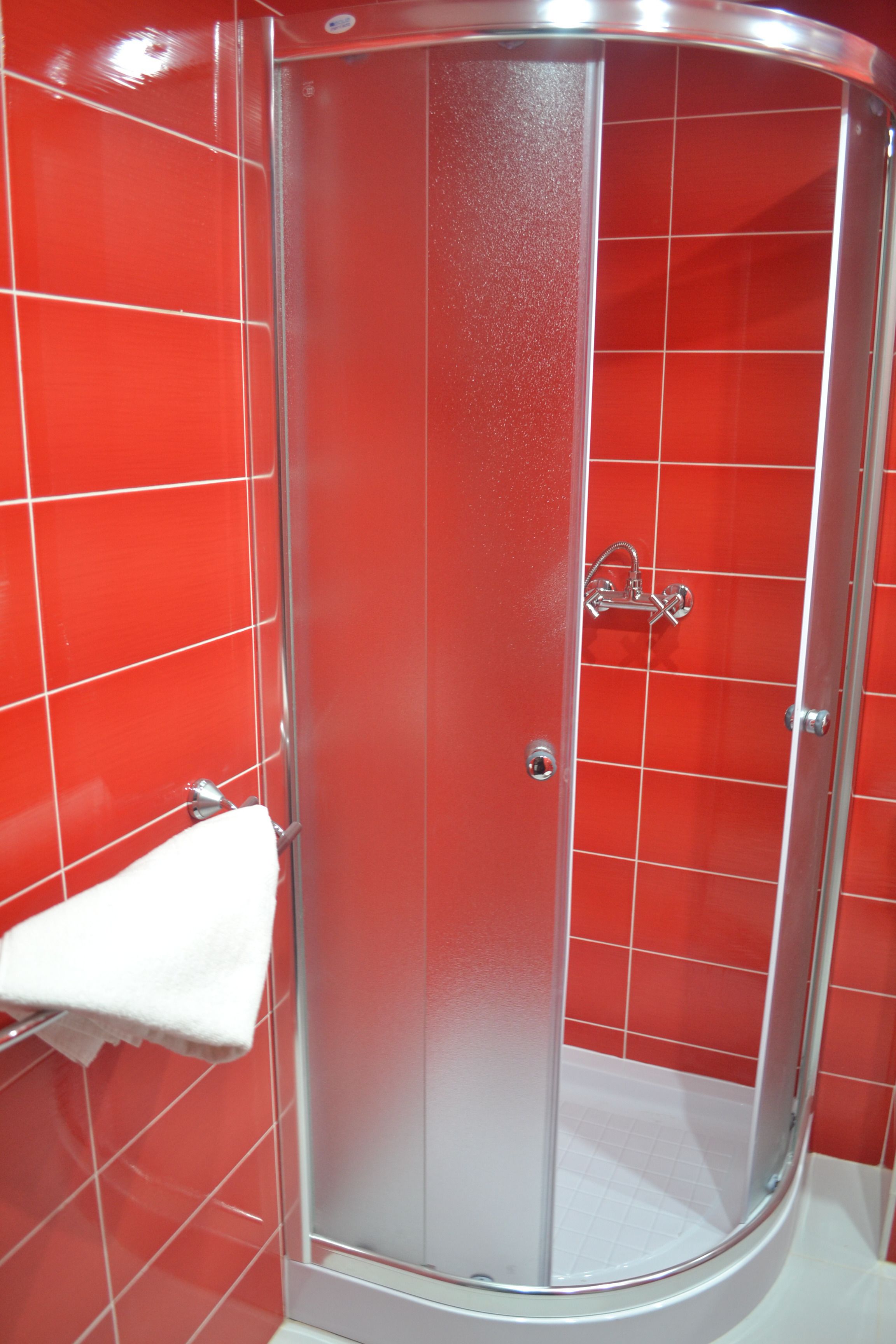 Une douche fermée par des parois de verre, avec une serviette blanche posée sur un porte-serviettes.