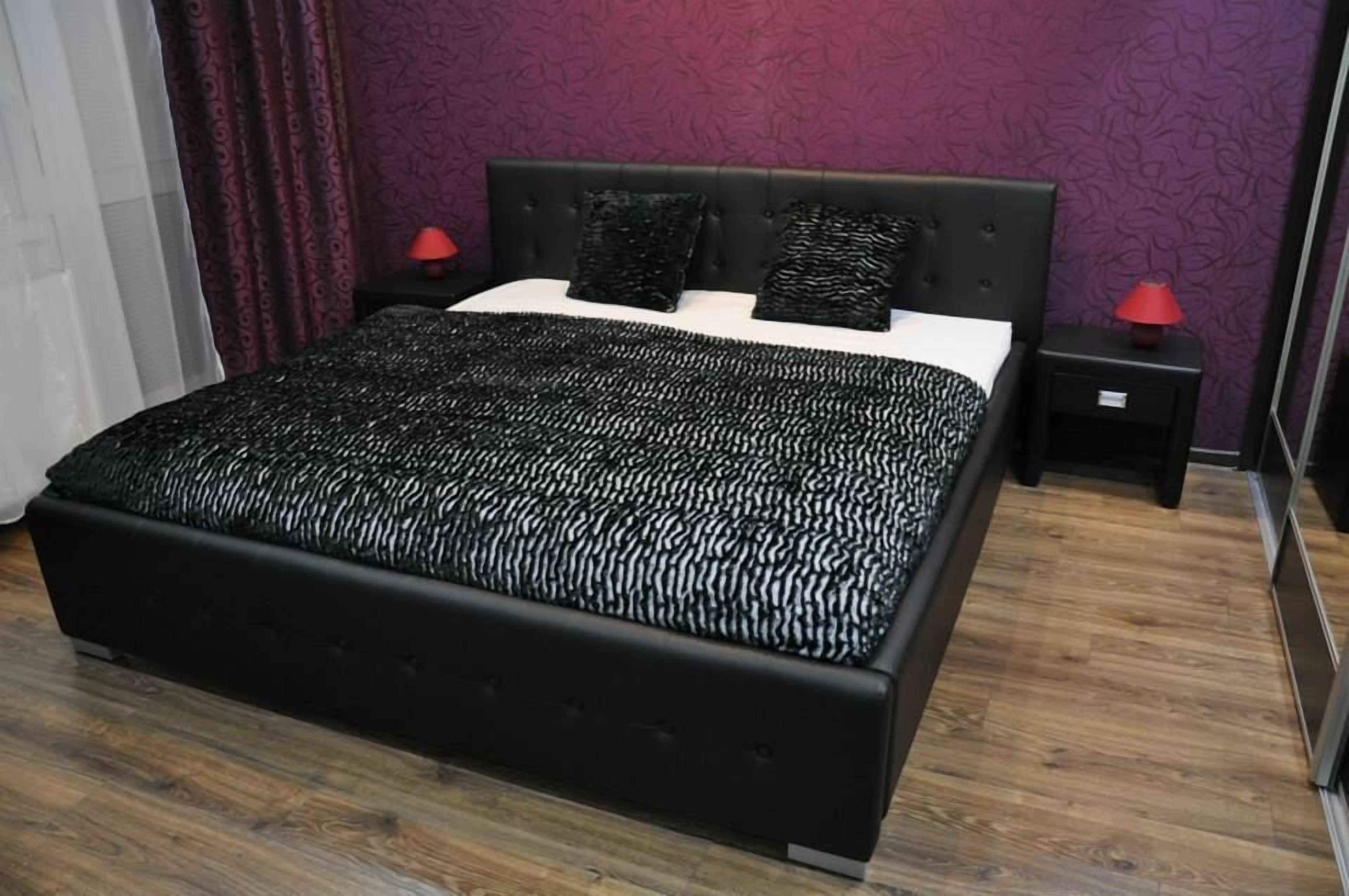 A modern bedroom with a large bed, dark headboard, and two nightstands with red lamps.