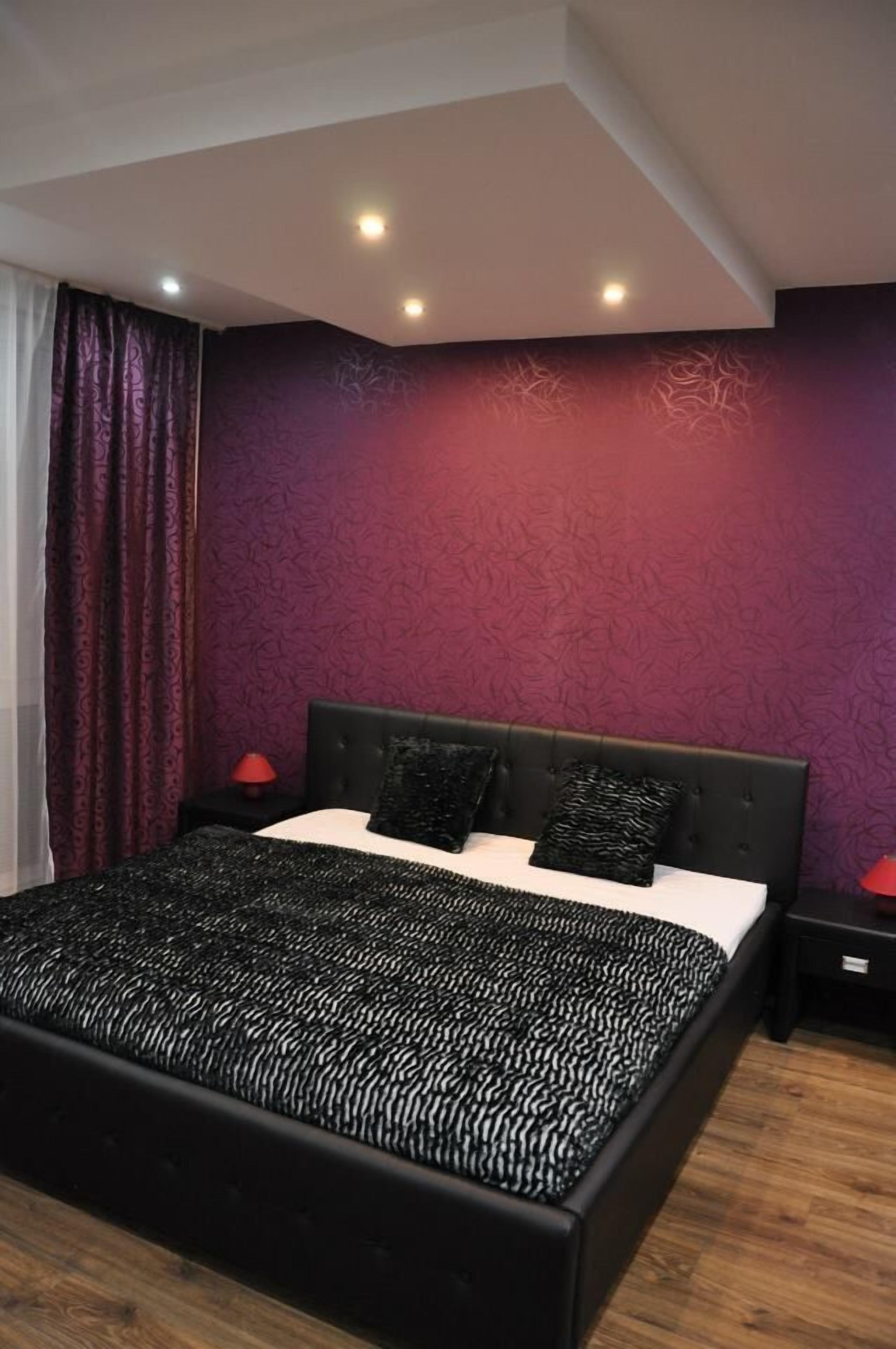 Un dormitorio moderno con una cama grande, cabecera oscura y paredes moradas.