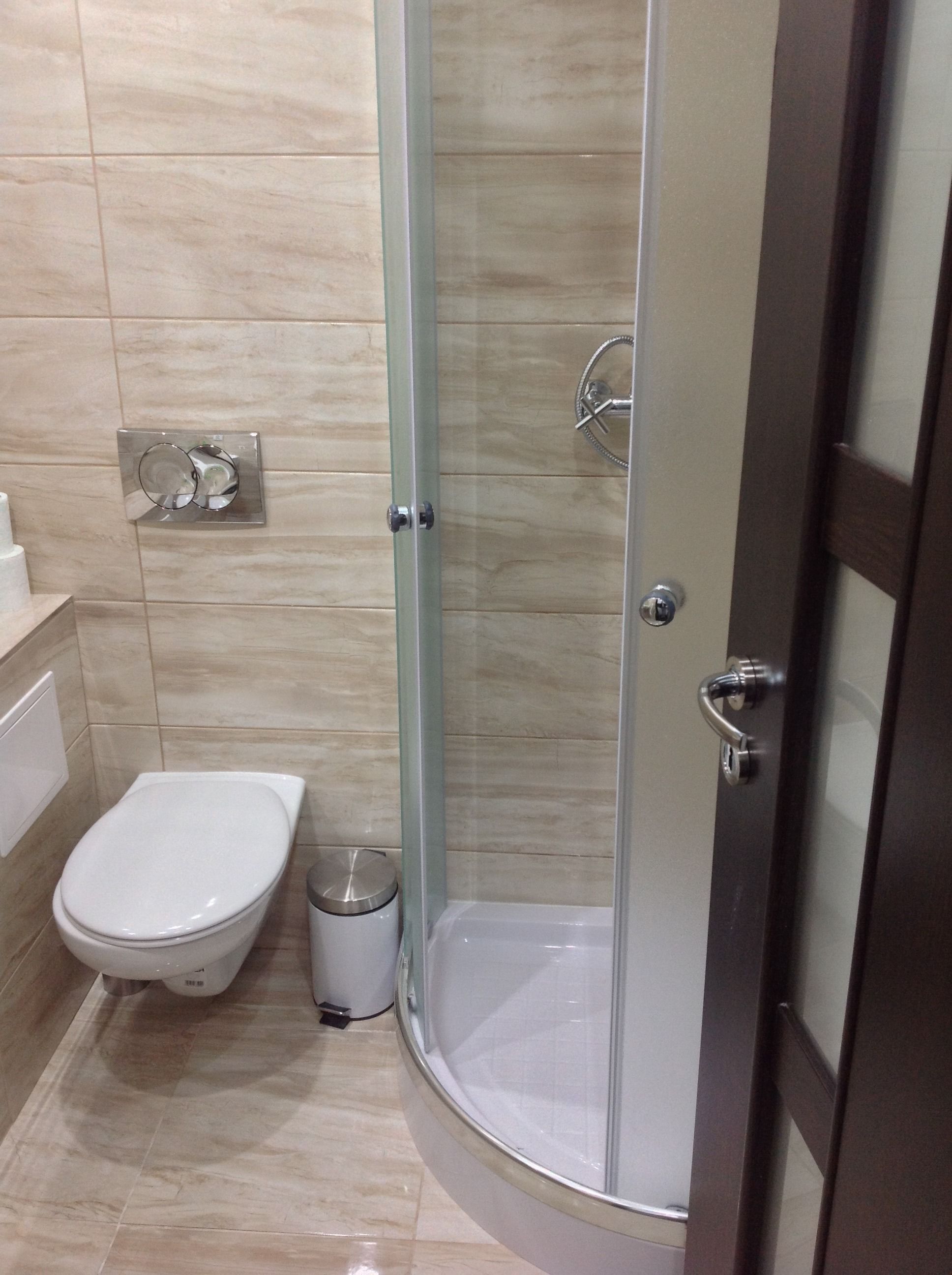 Un baño con inodoro, un cubo de basura y zona de ducha con mampara de vidrio.