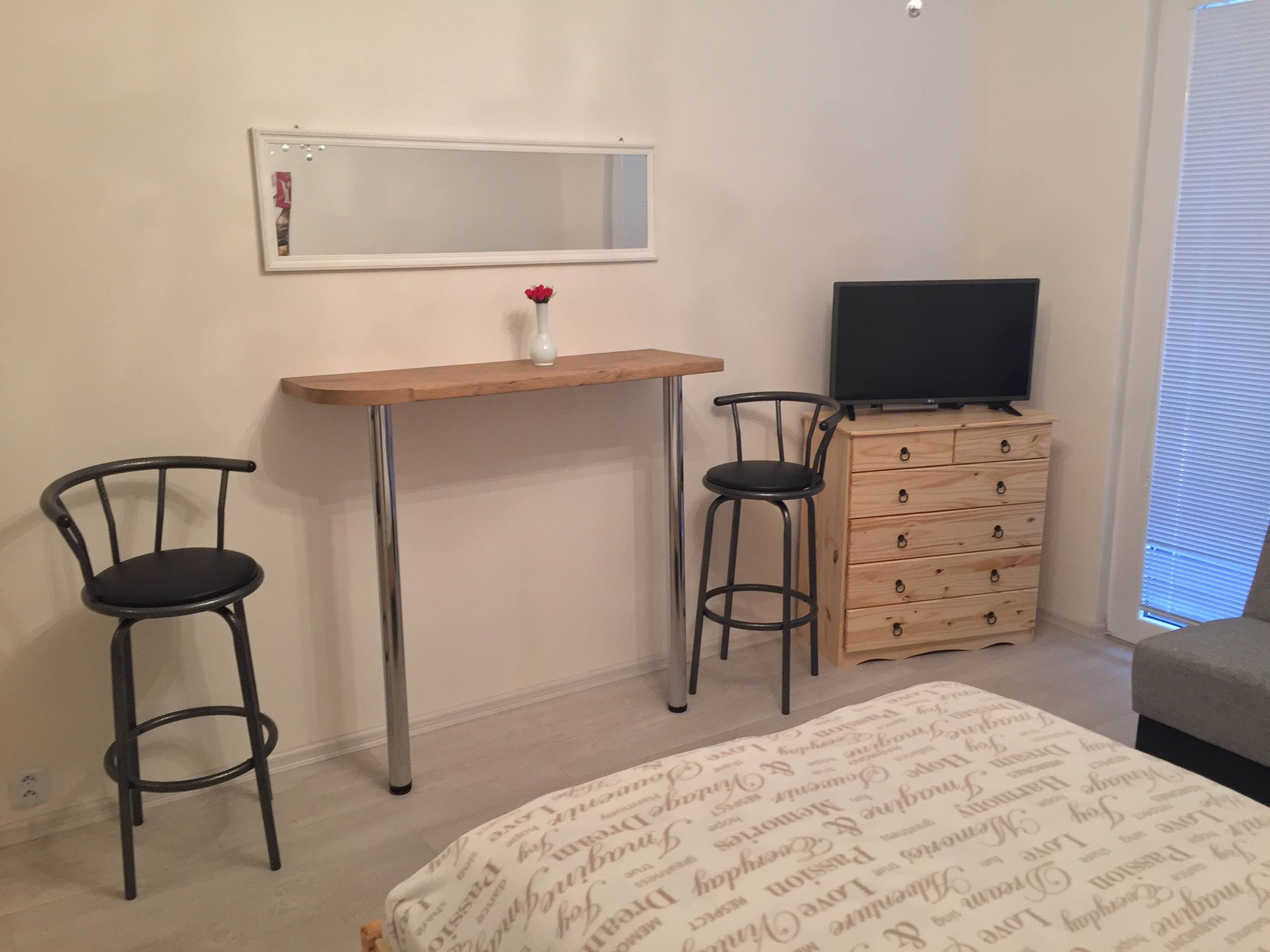 Ett sovrum med en säng, en byrå i trä, en tv och två stolar.