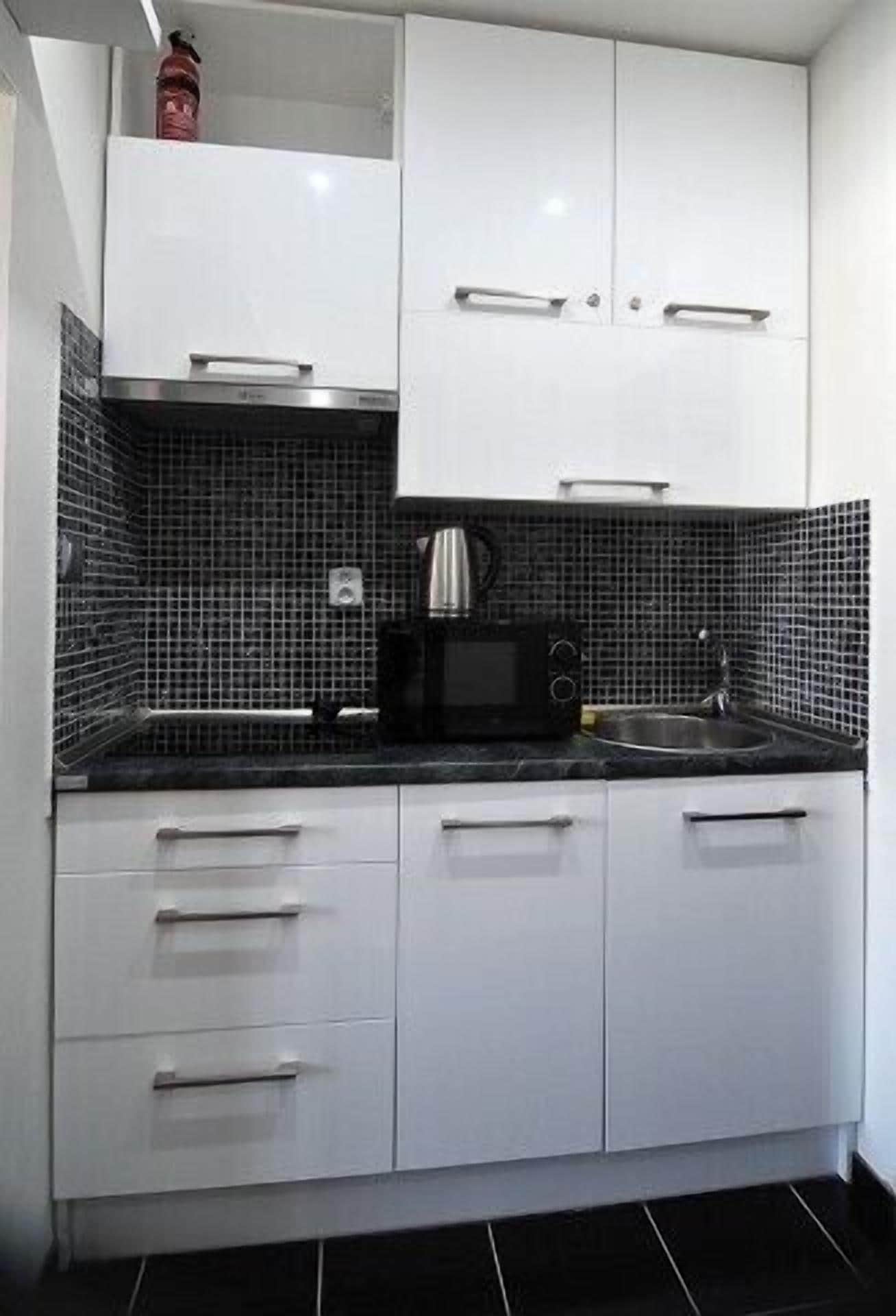 A compact kitchen with white cabinets, a black tiled backsplash, and a microwave.