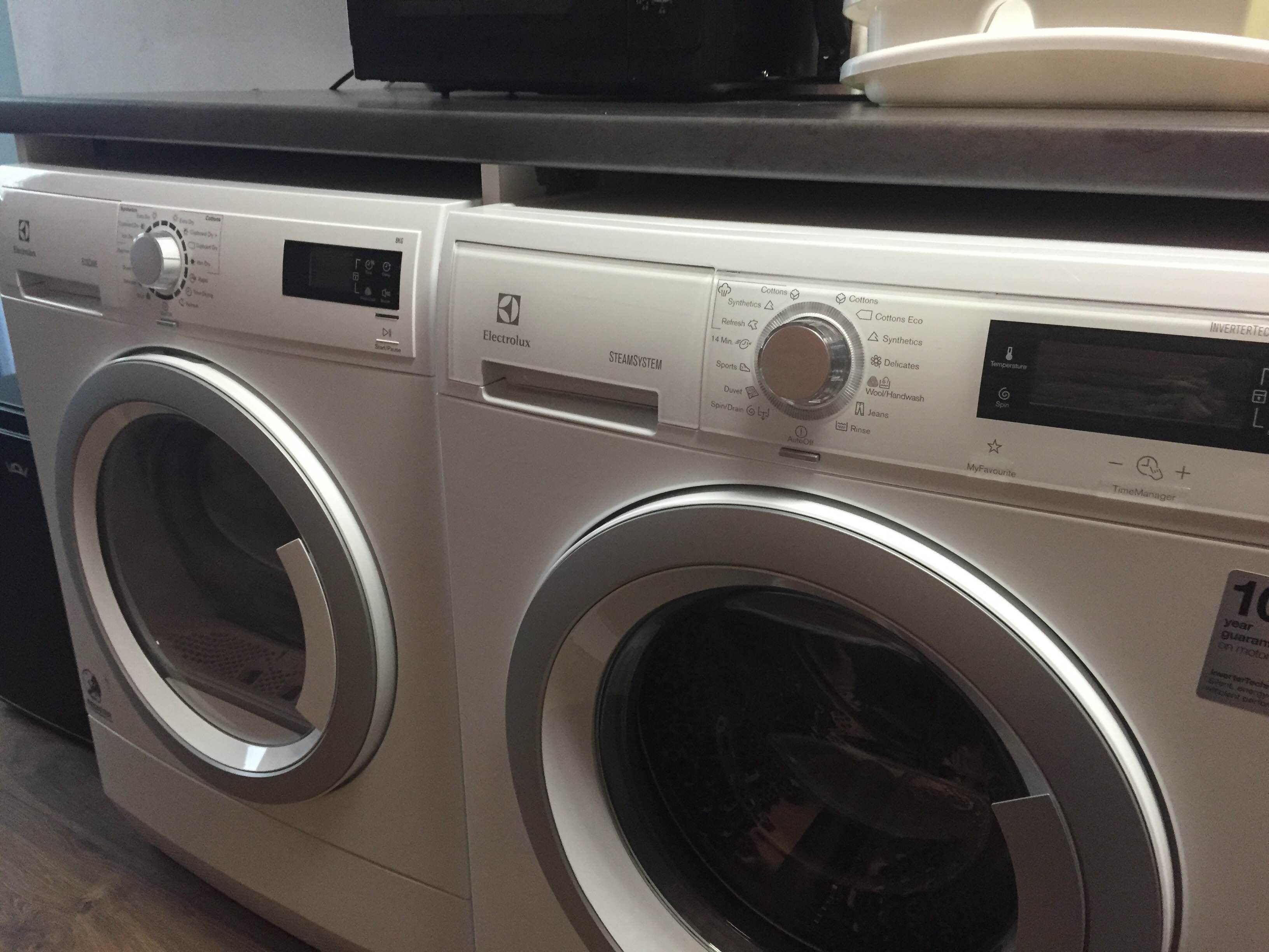 A front view of a modern, stainless steel front-loading washing machine with a digital display and control panel.