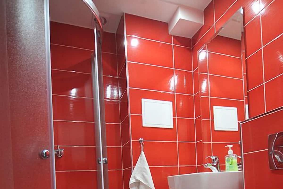 A bathroom with red tiled walls, a white sink, a toilet, and a glass shower enclosure.