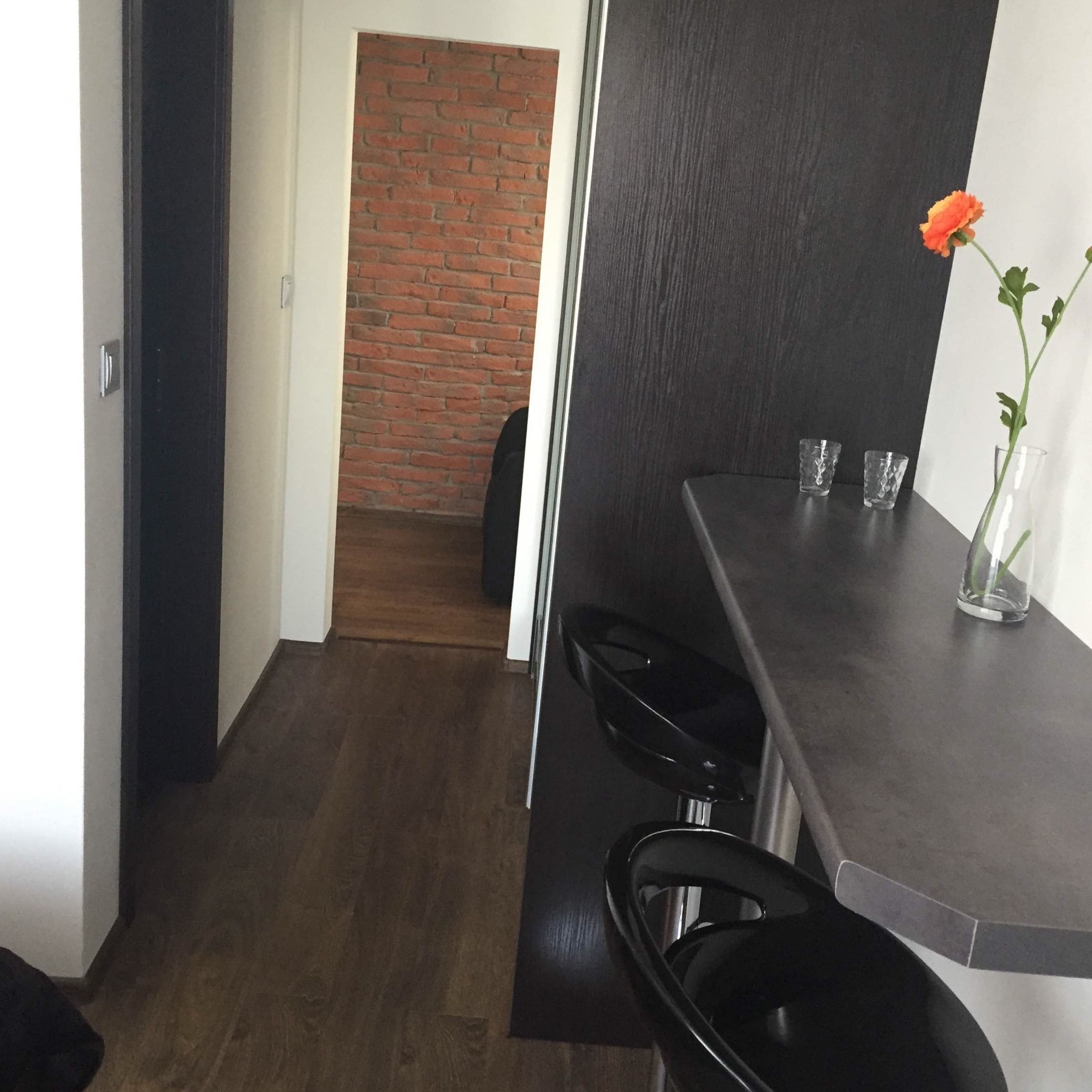 A modern kitchen with dark countertops, a black chair, and a vase with a single flower.