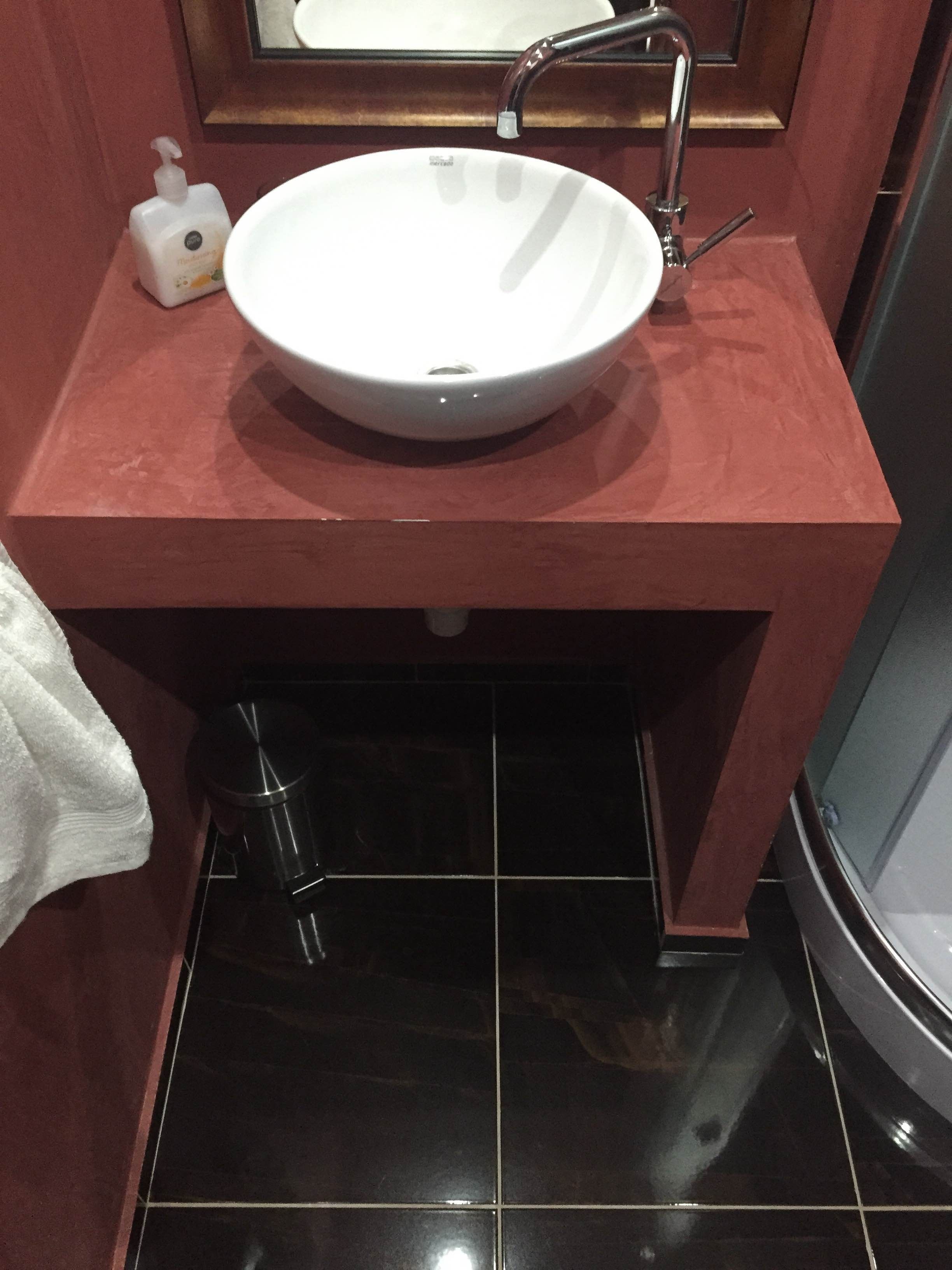 A bathroom with a white sink, a red countertop, and a mirror above it.