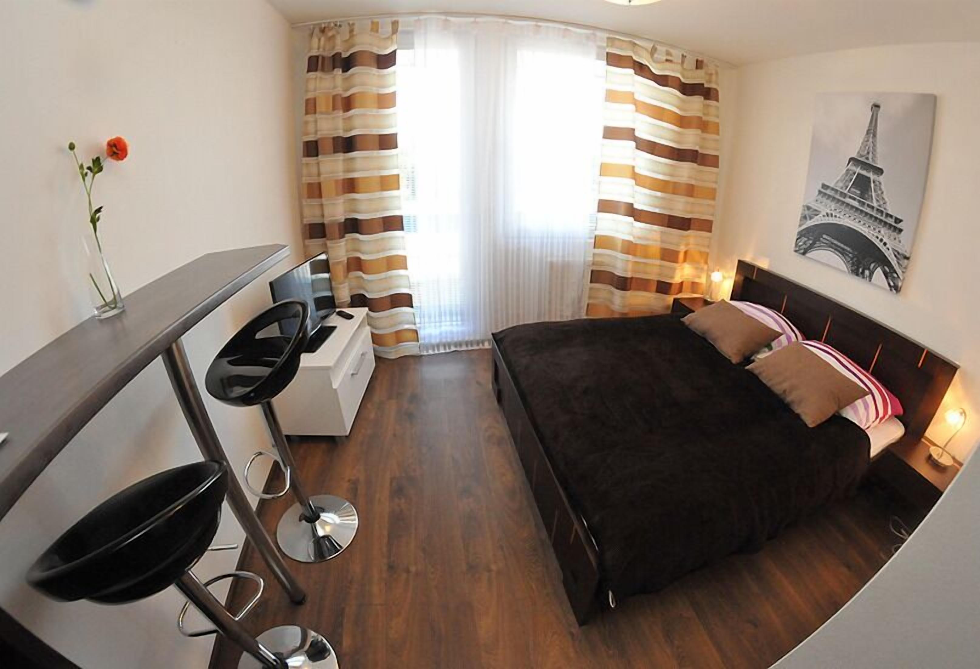Une chambre d’hôtel avec un lit, un bureau et une chaise, une petite table et une fenêtre avec des rideaux à rayures.