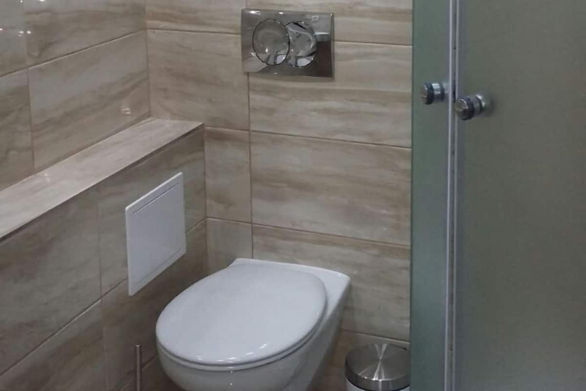 A modern bathroom with a toilet, a glass shower enclosure, and a trash bin.