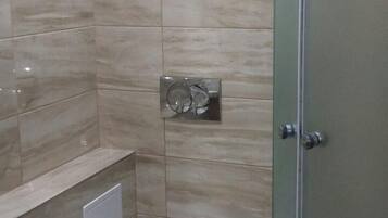 Un baño moderno con inodoro, cabina de ducha de vidrio y un cubo de basura.