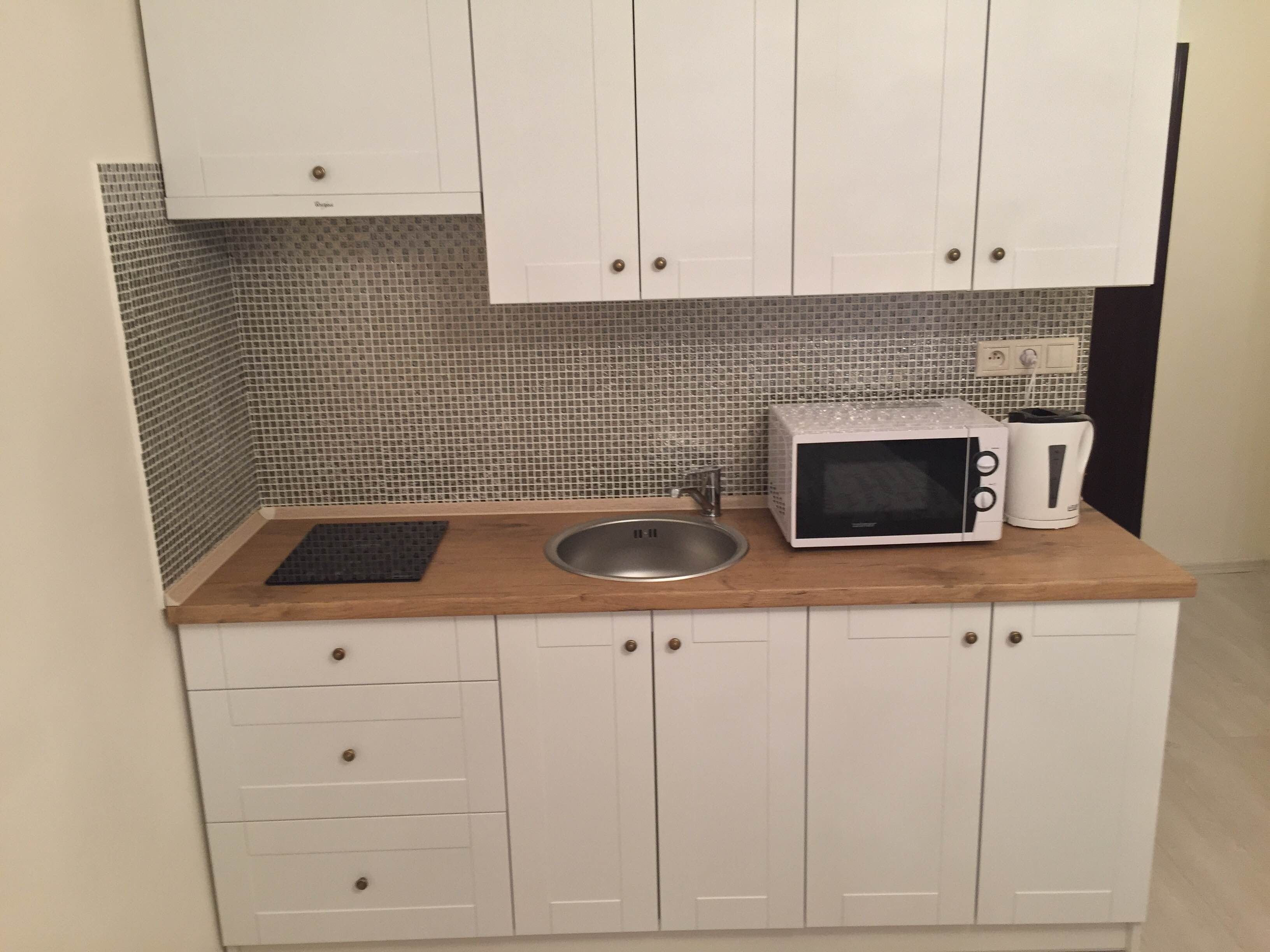 Een compact keukenhoekje met witte kastjes, een spoelbak, een magnetron en een waterkoker.