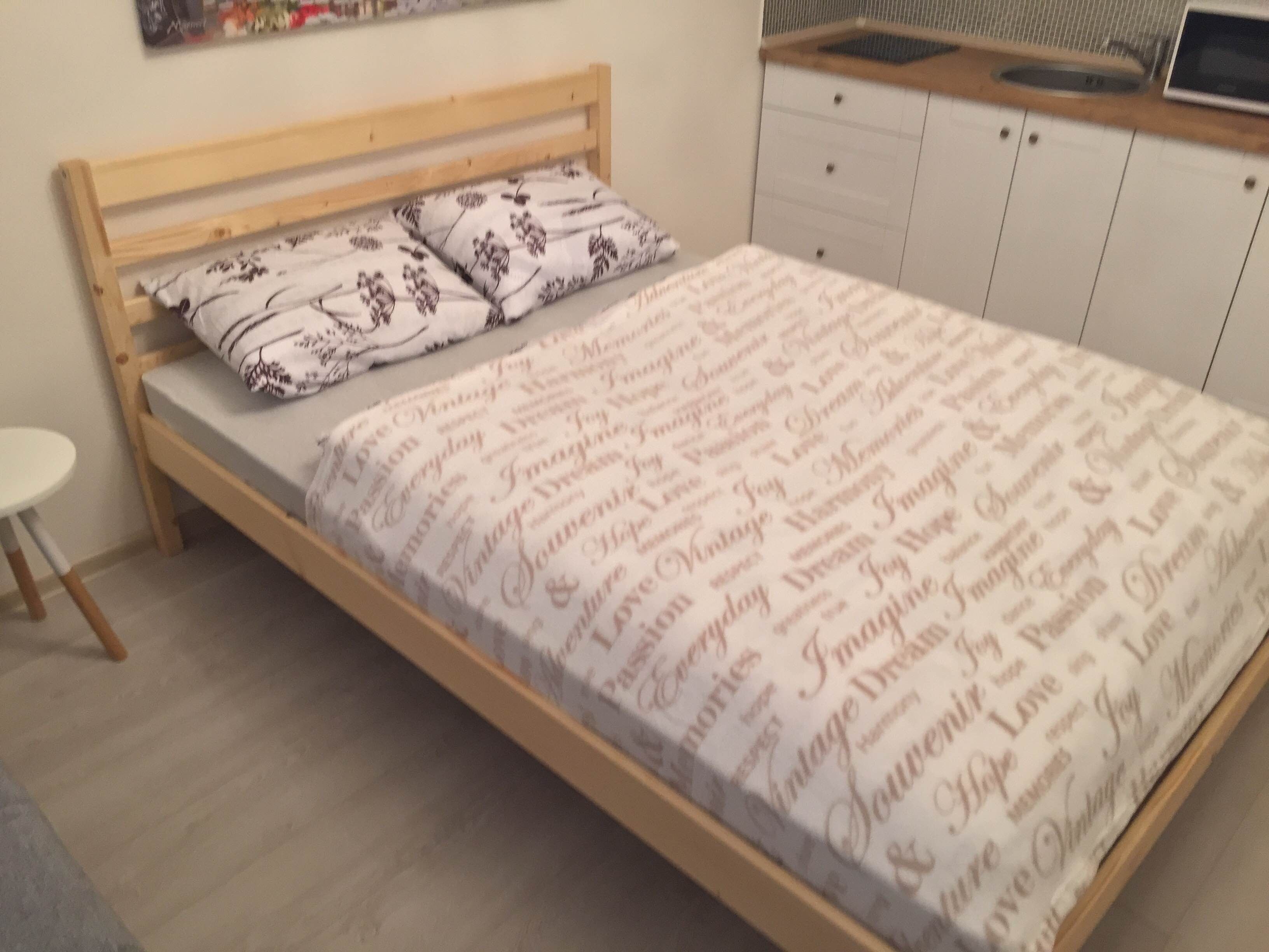 A bedroom with a wooden bed, patterned pillows, a white duvet, and a small bedside table.