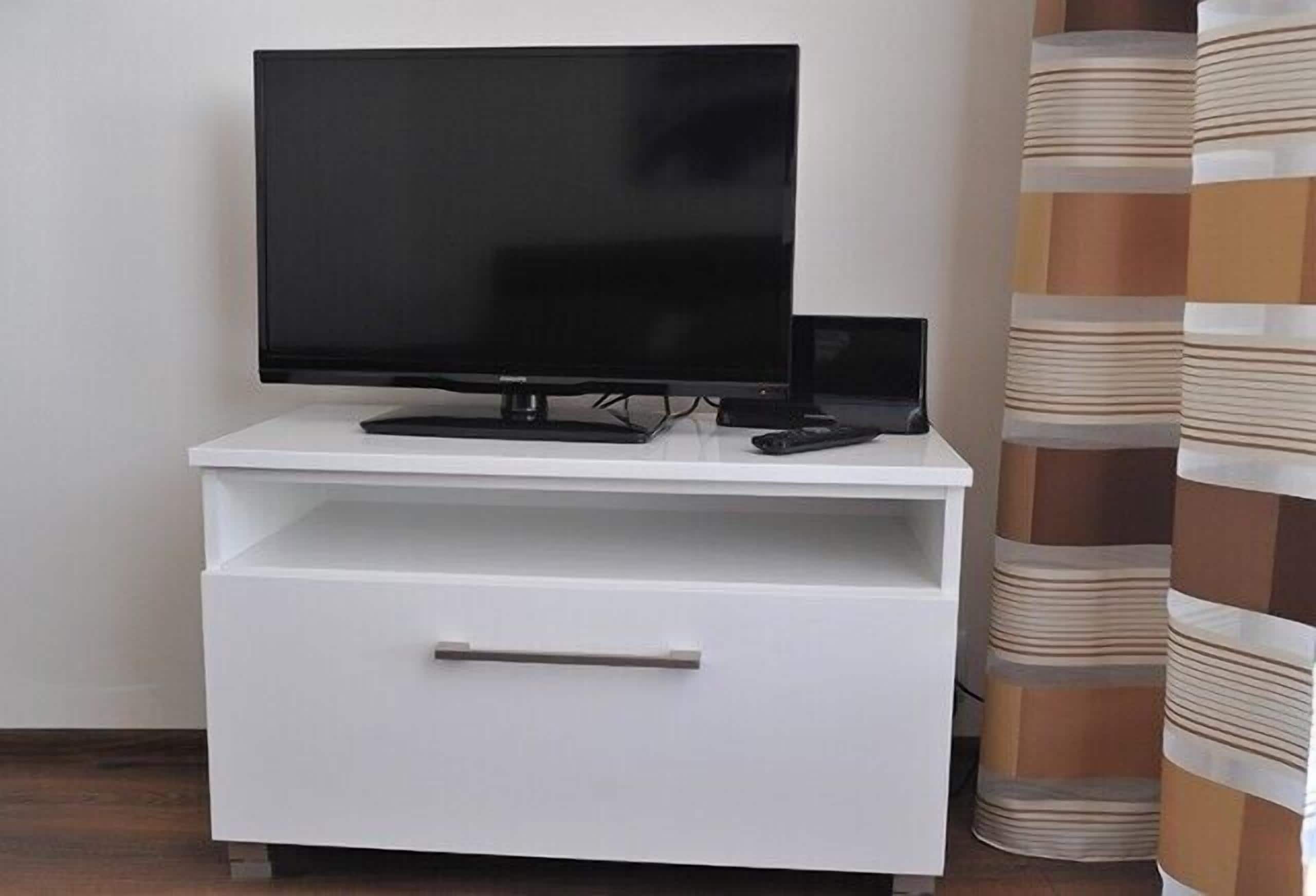 A white TV stand with a flat-screen TV and a remote control.