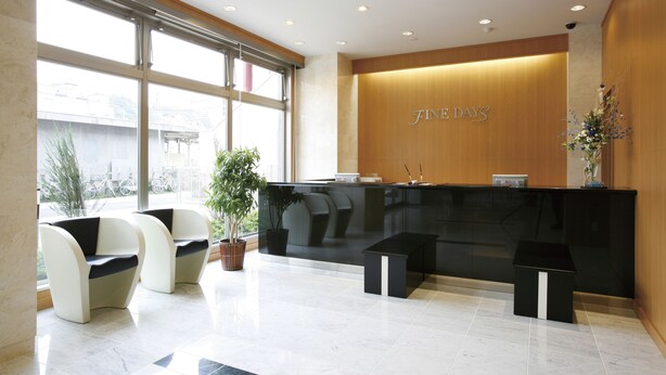 A reception area with a black reception desk, two white chairs, a potted plant, and a small black table. - Finedays Hotel (Ina)