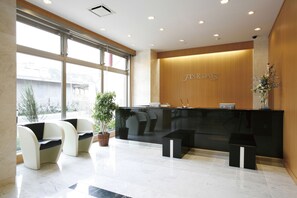A reception area with a black reception desk, two white chairs, a potted plant, and a small black table. - Finedays Hotel (Ina)