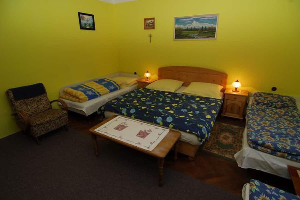 Una habitación con dos camas, una silla, una mesa y una cruz en la pared.