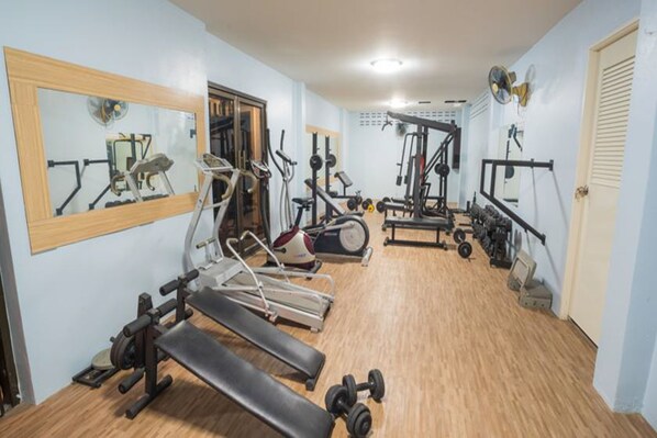 Un gimnasio con diverso equipamiento de ejercicio, incluyendo cintas de correr, una banca y pesas.