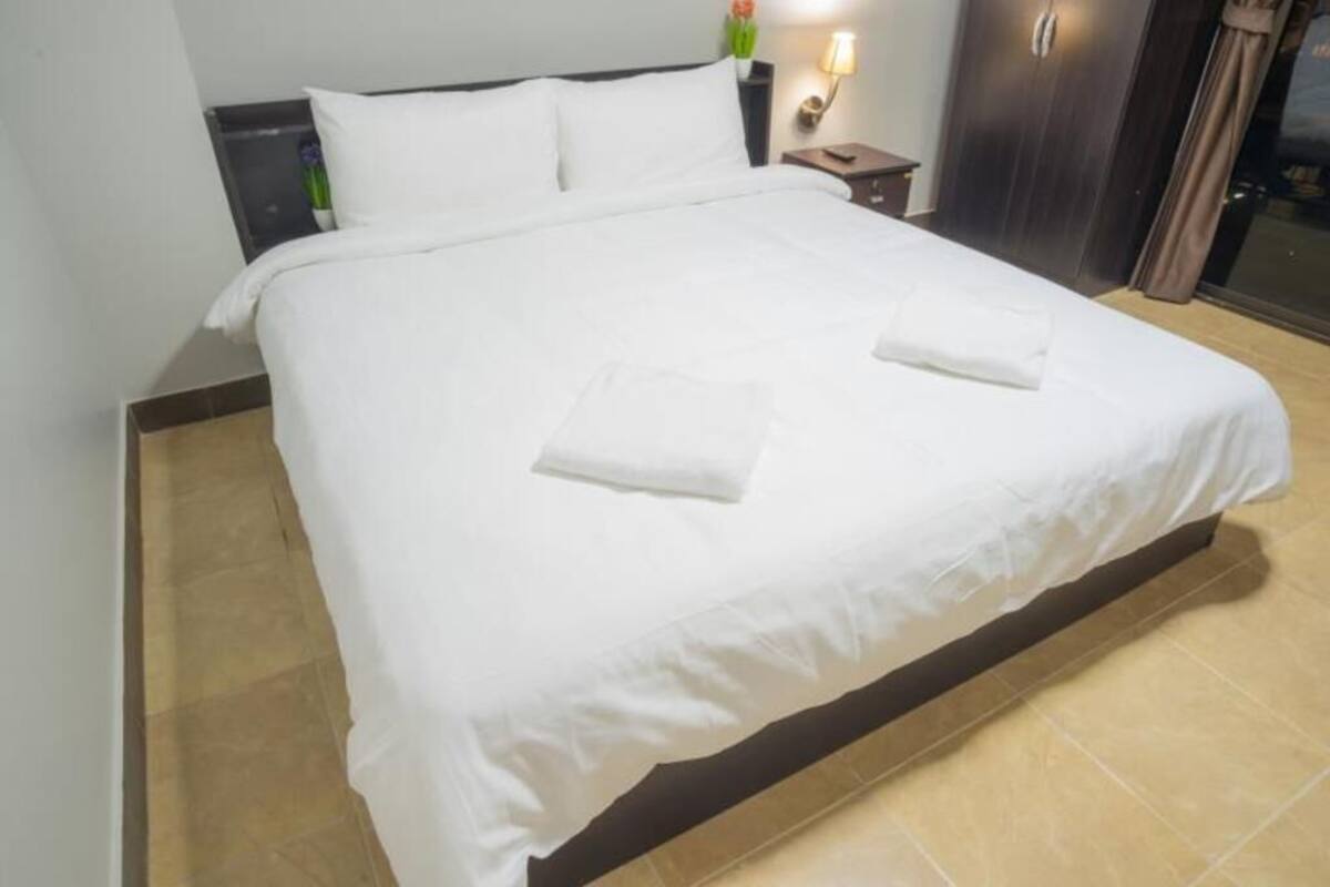 A neatly made bed with white linens, a bedside table with a lamp, and a dark wooden wardrobe.