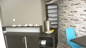Zona de recepción de un hotel con un mostrador de madera oscura, una máquina de café y una silla azul.
