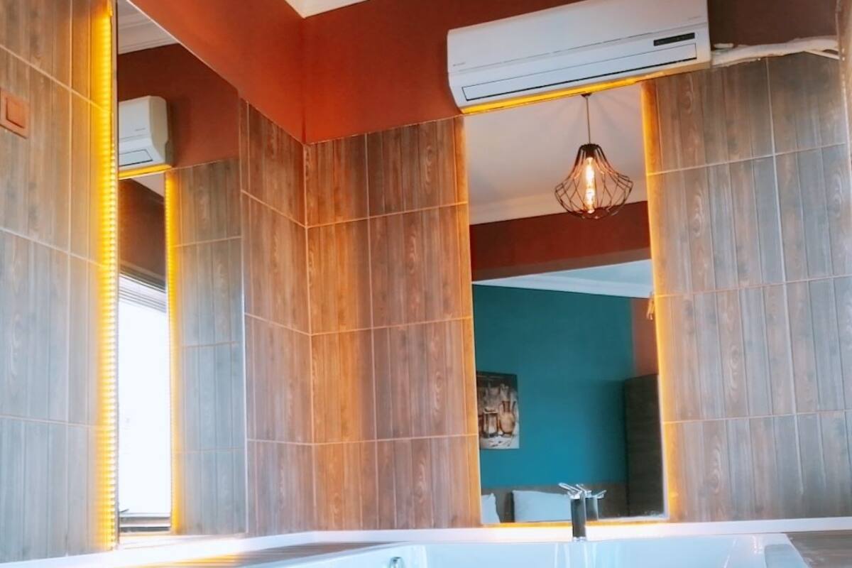 A modern bathroom with a wooden panel design, a glass-enclosed hot tub, and an air conditioning unit.