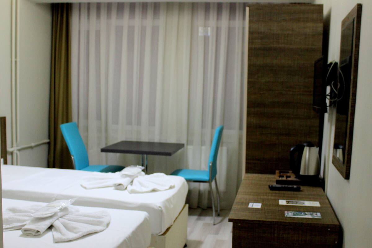 A hotel room with two beds, a small table, two chairs, a coffee maker, and a TV.
