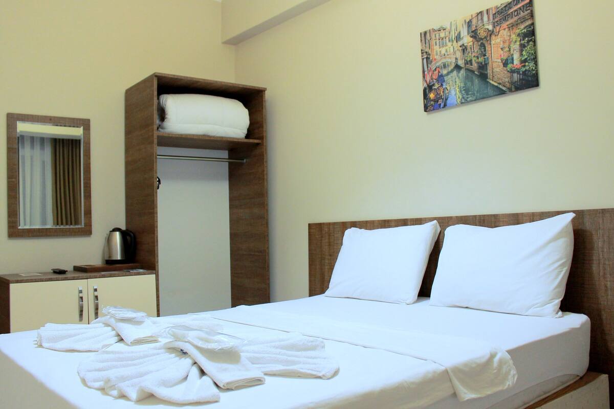 A hotel room with a neatly made bed, a wardrobe with a mirror, and a painting on the wall.
