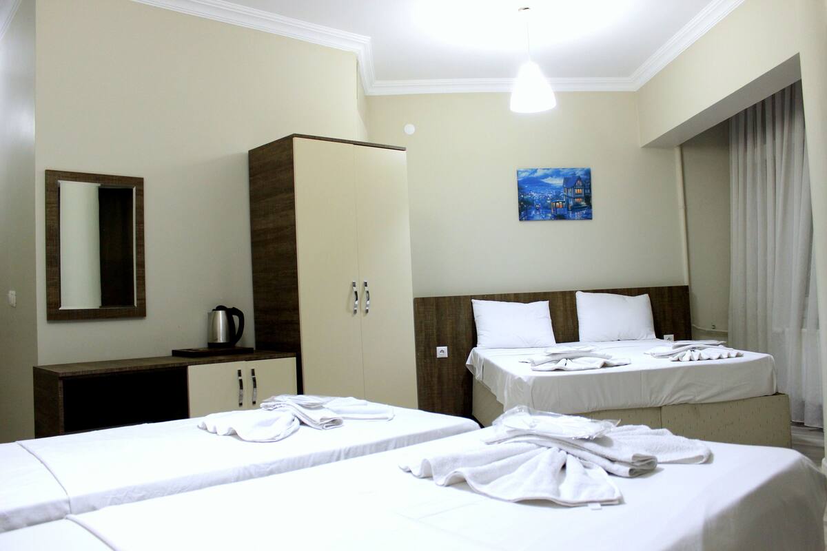 A hotel room with two beds, a wardrobe, a painting, and a window with curtains.