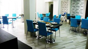 Comedor con sillas y mesas azules, piso de madera y pared con nombres de ciudades repetidos.