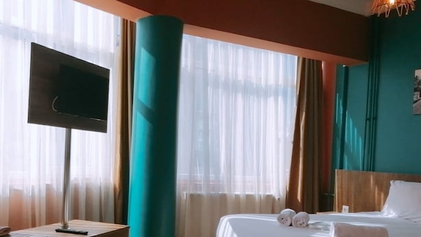 Habitación de hotel con cama, televisión, lavabo y un gran ventanal con cortinas.