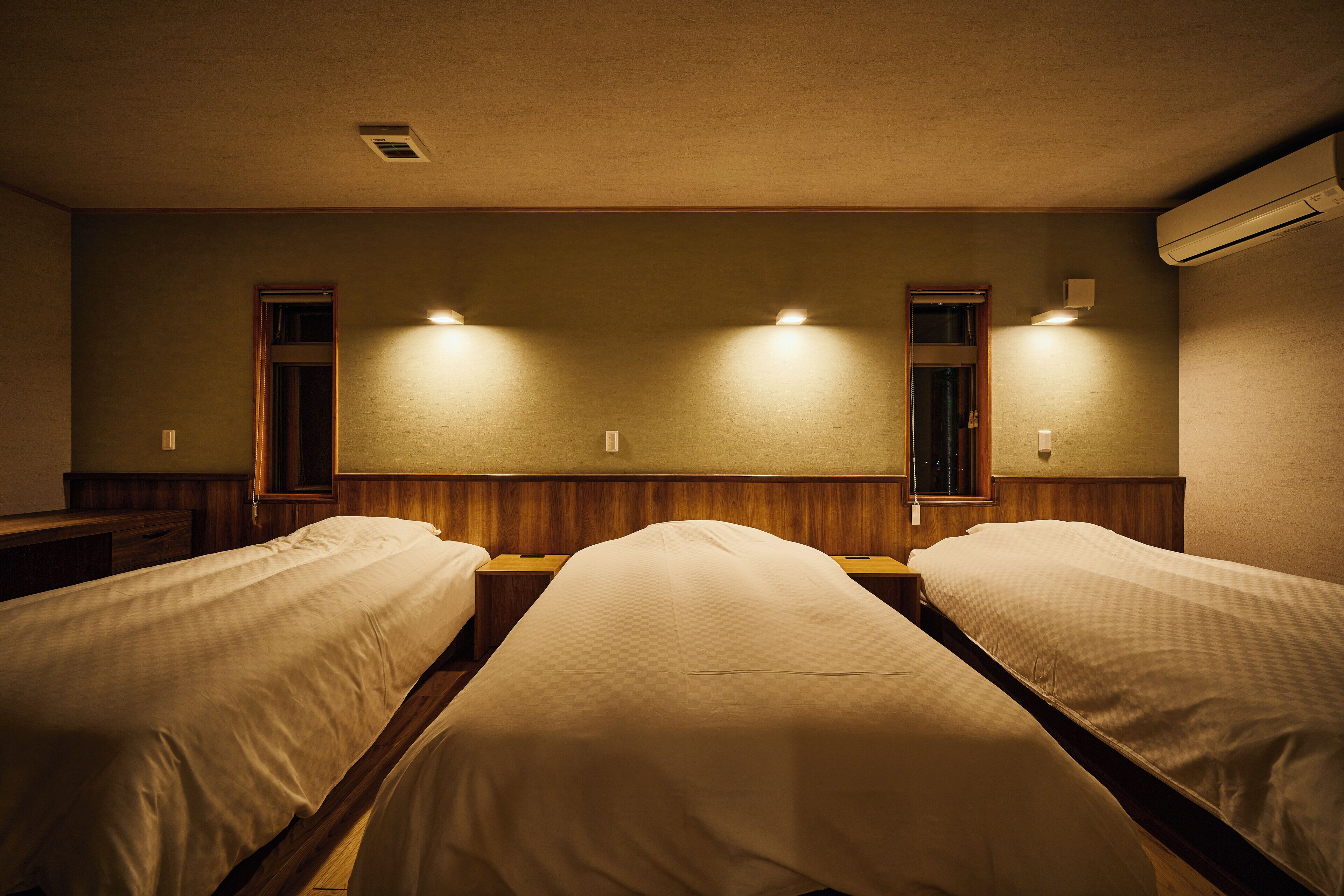 A hotel room with two single beds, wooden headboards, and built-in nightstands.