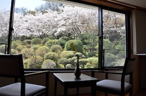 A room with a large window offering a view of a garden with cherry blossoms. - Shougen Sansou (Tamana)