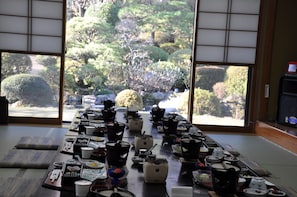 A traditional Japanese room with tatami flooring, a low table set with tea ceremony utensils, and a view of a lush garden through sliding doors. - Shougen Sansou (Tamana)