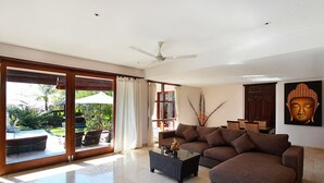 A spacious living room with a large sofa, a coffee table, and a ceiling fan. - Balangan Beach Villa (Jimbaran)