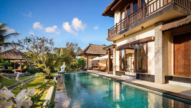 A swimming pool surrounded by tropical plants and a two-story building with a balcony. - Balangan Beach Villa (Jimbaran)