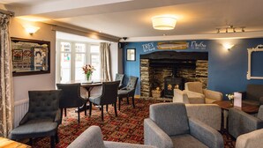 A cozy lounge area with comfortable seating, a stone fireplace, and a large window with curtains. - The Elan Hotel (Rhayader)