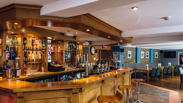 A bar area with a wooden counter, multiple liquor bottles, and a clock on the wall. - The Elan Hotel (Rhayader)