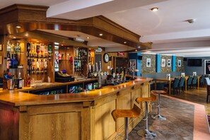 A bar area with a wooden counter, multiple liquor bottles, and a clock on the wall. - The Elan Hotel (Rhayader)